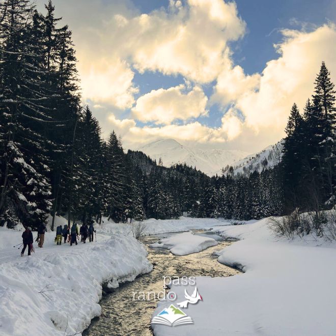 Photo de randonneurs marchant dans la neige le long d'une rivière dans une forêt de sapin